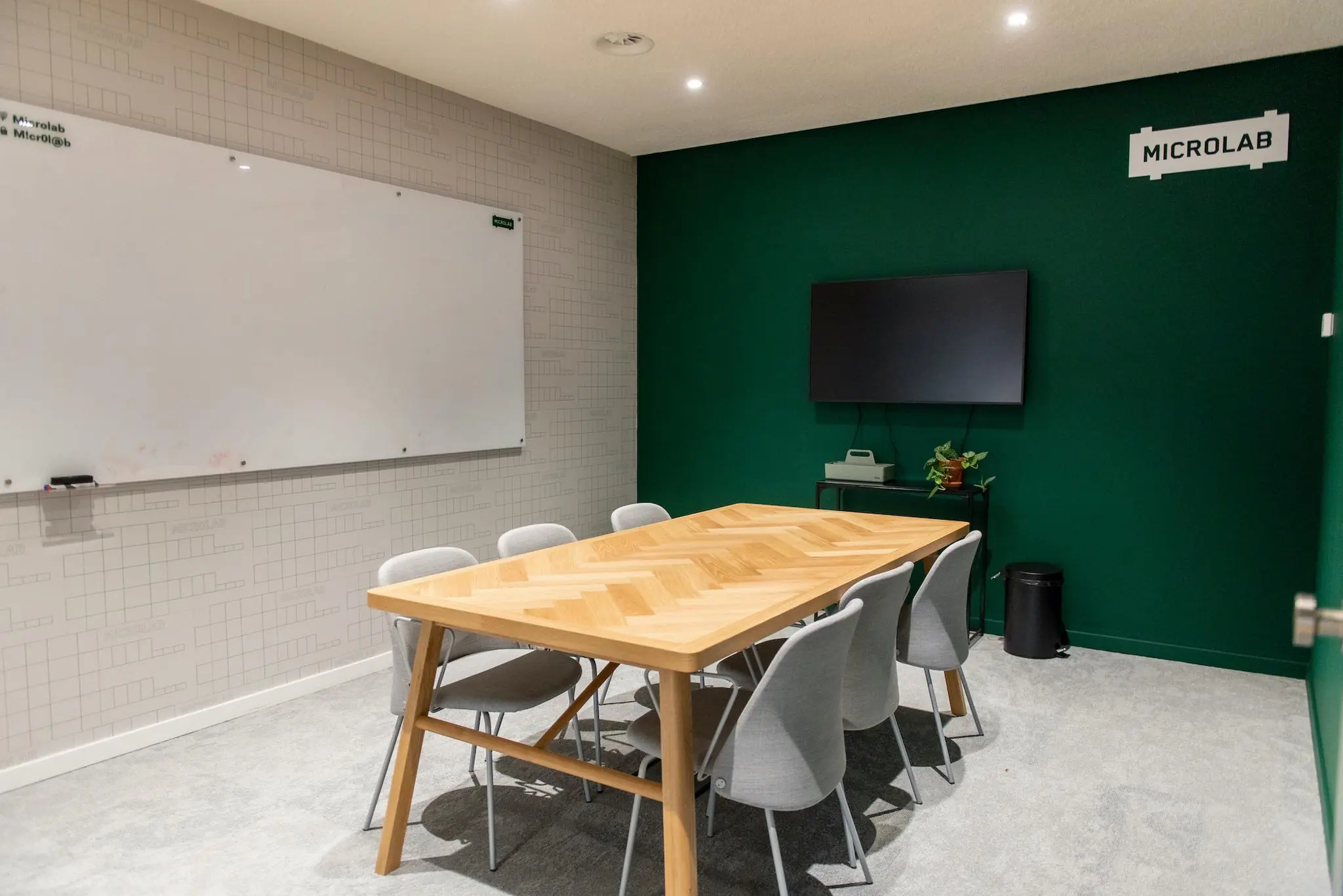 Vergaderruimte in Microlab aan de Aert van Nesstraat met houten tafel, grijze stoelen, whiteboard en scherm aan de muur.